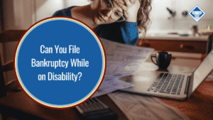 Image of a woman with a stressed expression, studying her bills with her laptop open and a black mug of coffee set to the side. The title of the article, "Can you file bankruptcy while on disability" is placed to the left of the image inside of a blue circle.