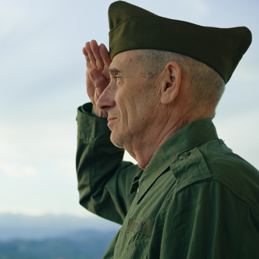 An older soldier is seen in profile saluting to someone off-screen.