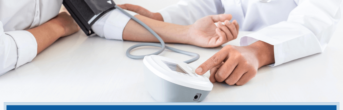 Photo of a doctor at a table with a patient taking the patient's blood pressure. Article title across the bottom of the picture: What is the VA Rating for Hypertension?