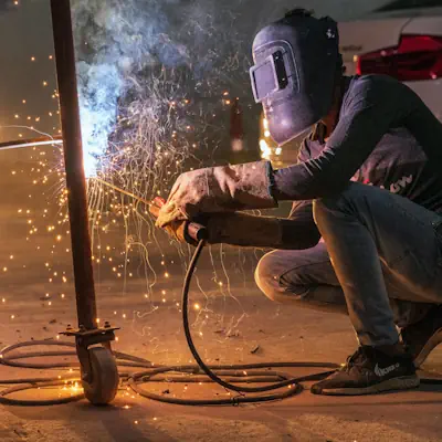 A person squatting to weld some steel pipes.